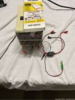 DC power supply unit connected with multiple test leads and clips on a white surface.
