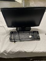 Front view of the LG monitor with Azio keyboard in front of it on a cloth surface. Keyboard has round keycaps and two keys missing.