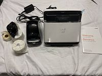Dymo label printer, rolls of white label tape, Neat scanner, power adapters, and user manual on white sheet