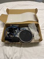 Top view of open box showing microphone, pop filter, cables, shock mount and foam windscreen inside packaging.