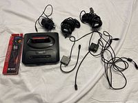 Sega Genesis console with Jeopardy cartridge, two black wired controllers, two RF units in original boxes, and power adapter laid out on white surface.