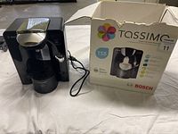 Front view of Bosch Tassimo T55 coffee maker with its original box placed beside it on a white cloth.