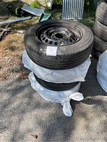 Side view of stacked tires wrapped in plastic with visible black steel rim and tread pattern.