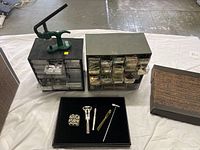 Full view of the kit including the green watch press, two plastic battery organizers with multiple drawers, and a black tray with watch repair hand tools.