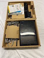 Opened box showing black Wii U console, GamePad, power cable, and instruction manuals inside cardboard compartments.