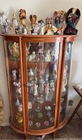 Wide view of wooden glass display cabinet housing numerous angel and other figurines on multiple shelves and the top surface.