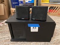 Front view of the two small satellite speakers placed on a large black bass module with a label '43 Bose' on it.