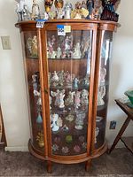 Full view of curved glass china cabinet with wood frame and glass shelves inside, showing scale and condition.