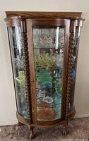 Front view of the wood and glass china cabinet showing the curved glass panels, display shelves, and carved twisted columns.