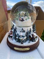 Large Thomas Kinkade Victorian Village snow globe with detailed winter village scene, pine trees, and wooden base with plaque.