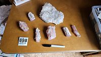 Overview of largest rock crystal cluster and six pieces of purple-hued petrified wood with marker and black marker for scale.