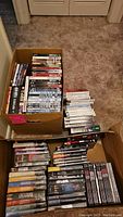 Photo showing multiple DVD box sets and individual DVDs in cardboard boxes on carpet.