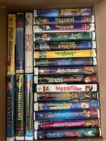 Box of VHS tapes and DVDs with children's animated titles including 'Lady and the Tramp', 'Beauty and the Beast', 'Bugs Life', and others.
