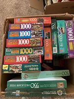 Top view of one box showing multiple Milton Bradley Hometown Collection puzzles with 1000 pieces each, some unopened.