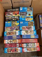 Stacked puzzle boxes showing various Americana themed puzzle designs and piece counts 300 to 1000 pieces. Many boxes new/unopened.