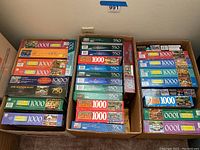 Three large boxes filled with multiple vintage Americana themed jigsaw puzzles with piece counts ranging from 500 to 1000 pieces.