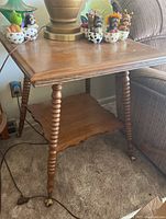 Full view of the wood side table showing top surface, spindle legs, and metal claw feet; placed on carpet next to a couch and lamp.