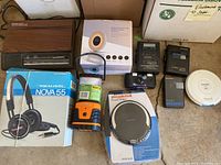 Photo showing assortment of vintage media electronics including phones, answering machines, headphones, CD players, cassette players, and a lantern