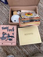 Top-down photo of stack of 45 RPM records in their paper sleeves, with vintage pink Tune Tote folder, and a yellow record folder labeled 'RECORDS'