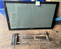 Front view of 42 inch Samsung plasma display and disassembled wall mount brackets laid out on wooden floor.