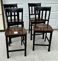 Four Ashley Furniture wooden bar stools with dark brown seats and black legs and backs shown together on concrete.