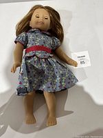 Full body photo of the 18 inch doll lying down wearing a blue floral dress with red trim, showing the overall doll condition and outfit details.