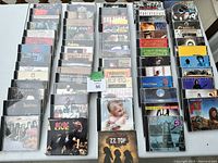 Overhead photo showing multiple stacks of classic rock CDs, featuring album covers of Eric Clapton, Jimi Hendrix, Doobie Brothers, Robert Cray, The Cult, Van Halen, ZZ Top, AC/DC and others.
