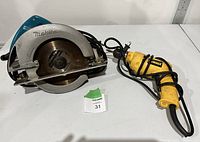 Makita circular saw and Dewalt drill placed on table with power cords visible.