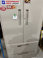 Front view of the metal workshop cabinet showing two doors and two drawers with automotive stickers on doors.