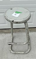 Full view of old metal stool showing round seat, tubular frame and footrest, paint worn and chipped.