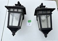 Pair of black outdoor wall lamps with textured glass lenses, front view showing both lamps laying on a flat surface.