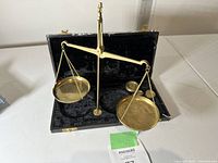 Brass balance scale with two hanging pans on a central stand, displayed inside an open case.