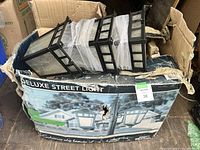 Box with the deluxe street light partially visible inside, showing three black lantern style light fixtures and packaging.