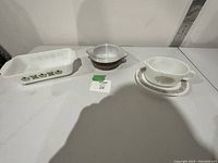 Photo showing three dishes: Fireking loaf pan with green floral pattern, Pyrex brown Woodland casserole with lid, and Pyrex Woodland gravy boat with saucer.