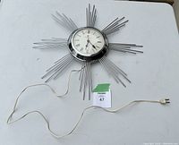 Full view of the sunburst wall clock including power cord and plug on white surface.