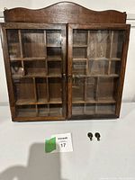 Front view of the wooden display case with glass double doors and original hooks placed in front.