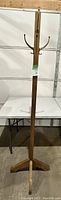 Full upright view of wooden tree coat rack stand with four vertical sides and multiple metal hooks.