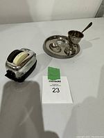 Photo showing the vintage salt and pepper dispenser shaped like an old toaster alongside the metal egg serving tray with glass dish and spoon on a white surface.