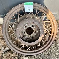 Rusty vintage metal car wheel rim with wire spokes and bolt holes in the center, showing heavy rust and outdoor wear.