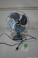 Front angle view of the blue vintage electric fan showing its blades, base, and power cord.