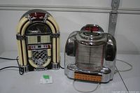 Photo showing both vintage style radios side by side, one jukebox design and one chrome radio with lettered dial.