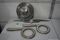 The lot items arranged on a table showing the chrome hub cap, car emblem, and two painted bicycle chain guards.