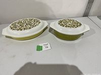 Two Pyrex Verde pattern casserole dishes with lids, side by side on a white surface.