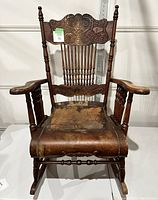Front view of vintage wooden rocking chair showing leather seat and turned armrests.