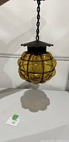 Hanging vintage amber glass bubble light with metal cage and chain seen from front side.