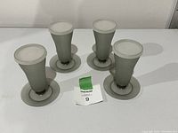 Four gray vintage Tupperware Sunday glasses with matching lids arranged upright on a white surface, showing clear view of each glass and lids.