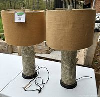 Pair of two wooden lamps with fabric shades shown on a table outdoors.