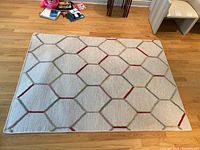 Area rug laid flat on the floor showing hexagonal geometric pattern with beige background and green and red accents
