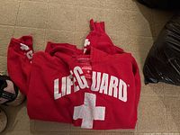 Red Lifeguard hooded sweater folded on carpet