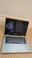 Open Dell Inspiron laptop showing keyboard and screen, silver body with black keys.